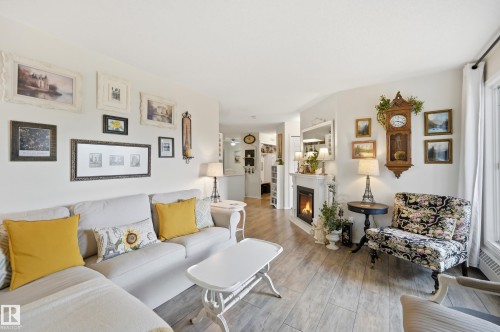 Living area featuring a fireplace with a white mantel, wood-finish flooring, and white walls - #208 9760 176 St Nw, Edmonton, AB - Indoor Photo Showing Living Room With Fireplace