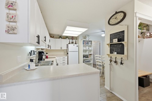Bright kitchen featuring white cabinetry with black hardware, a stainless steel sink with a high-arc faucet, and an overhead skylight - #208 9760 176 St Nw, Edmonton, AB - Indoor Photo Showing Kitchen With Double Sink