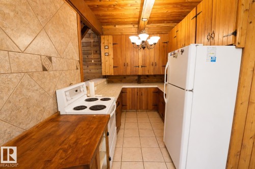 Kitchen featuring extensive wood-paneled walls and ceiling, U-shaped countertop layout, tile flooring, and integrated wall-mounted cabinetry - 329 60417 Range Road 124, Rural St. Paul County, AB - Indoor Photo Showing Kitchen