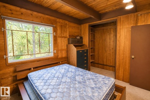 Bedroom featuring extensive wood-paneled walls and ceiling, a large window with security bars, and an open closet with built-in shelving and hanging rod - 329 60417 Range Road 124, Rural St. Paul County, AB - Indoor Photo Showing Bedroom