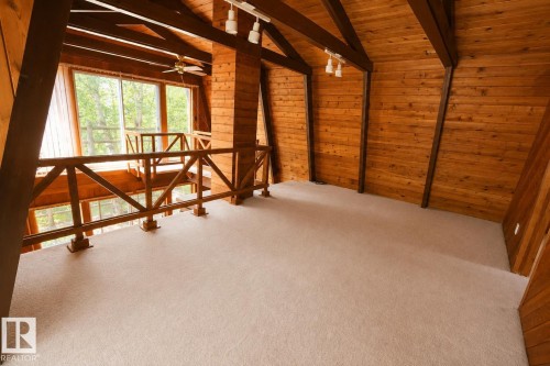 Carpeted loft area with wood-paneled walls and ceiling, exposed structural beams, track lighting, and a wood railing overlooking the lower level with large windows - 329 60417 Range Road 124, Rural St. Paul County, AB - Indoor Photo Showing Other Room