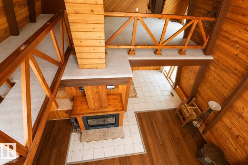 Interior featuring a wood-burning fireplace with a tile hearth, wood-finish flooring, and a second-story open-concept area with wood railings - 329 60417 Range Road 124, Rural St. Paul County, AB - Indoor Photo Showing Other Room With Fireplace