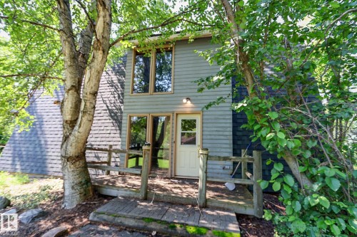 Exterior featuring a light-colored entry door, an outdoor wall sconce, and a wood-finish deck with railings - 329 60417 Range Road 124, Rural St. Paul County, AB - Outdoor