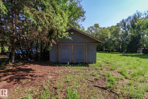 Detached outbuilding with an A-frame roof and dual wooden doors, set on a grassy parcel with mature trees - 329 60417 Range Road 124, Rural St. Paul County, AB - Outdoor