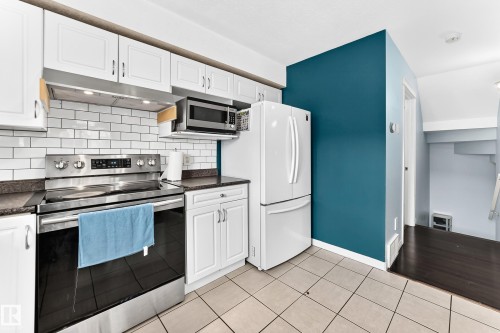 Kitchen featuring white cabinetry, subway tile backsplash, stainless steel range with overhead microwave, and neutral-toned floor tiling - #72 2505 42 St Nw, Edmonton, AB - Indoor Photo Showing Kitchen