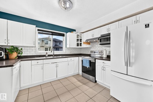 Kitchen featuring white cabinetry, dark countertops, a subway tile backsplash, stainless steel appliances, and a window above the sink - #72 2505 42 St Nw, Edmonton, AB - Indoor Photo Showing Kitchen With Double Sink With Upgraded Kitchen