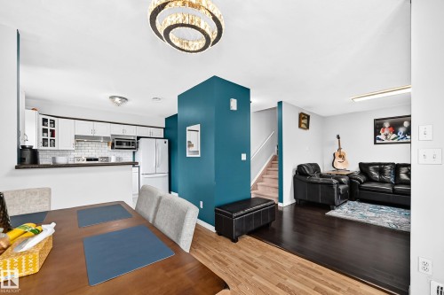 Open-concept living space featuring a modern kitchen with white cabinetry and subway tile backsplash, a dining area with a contemporary chandelier, and rich wood-finish flooring - #72 2505 42 St Nw, Edmonton, AB - Indoor
