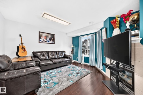 Living area featuring dark wood-finish flooring, a contemporary rectangular ceiling light fixture, and a bay window with natural light - #72 2505 42 St Nw, Edmonton, AB - Indoor Photo Showing Living Room