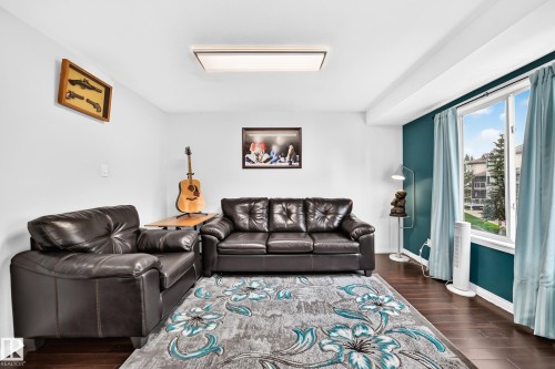 Living area with dark wood-finish flooring, white walls, and an accent wall in a deep teal hue - #72 2505 42 St Nw, Edmonton, AB - Indoor Photo Showing Living Room