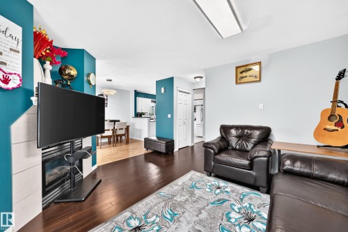 Living area featuring wood-finish flooring, a corner fireplace with light-toned tile surround, and a ceiling-mounted light fixture - #72 2505 42 St Nw, Edmonton, AB - Indoor Photo Showing Living Room