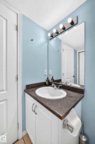 Bathroom vanity featuring white cabinetry with silver pulls, an integrated basin, a speckled countertop, and a large wall-mounted mirror - #72 2505 42 St Nw, Edmonton, AB - Indoor Photo Showing Bathroom