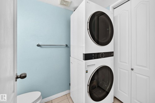 White stackable washer and dryer unit with front-loading design, complemented by a nearby two-panel white bifold closet door - #72 2505 42 St Nw, Edmonton, AB - Indoor Photo Showing Laundry Room