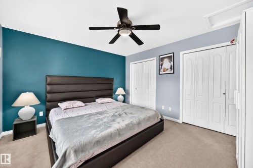 Carpeted bedroom featuring a dark-toned upholstered headboard, multiple closet doors, and a ceiling fan with integrated lighting - #72 2505 42 St Nw, Edmonton, AB - Indoor Photo Showing Bedroom