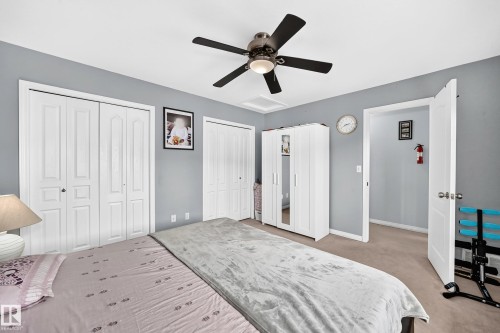 Bedroom featuring two bi-fold closets with panel detailing, a ceiling fan with integrated lighting, soft gray wall tones, and neutral-toned carpeting - #72 2505 42 St Nw, Edmonton, AB - Indoor Photo Showing Bedroom