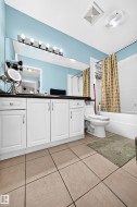 Bathroom featuring a white vanity with dark countertop, large wall-mounted mirror, overhead vanity lighting, white bathtub, and tile flooring - 