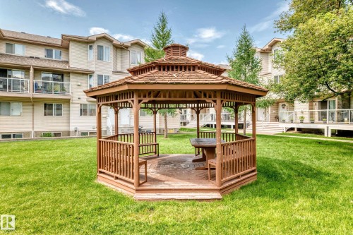 Central wooden gazebo featuring built-in benches and a hexagonal table, surrounded by a green lawn - #72 2505 42 St Nw, Edmonton, AB - Outdoor With Deck Patio Veranda With Backyard
