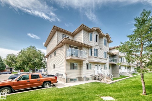 Multi-story residential building featuring light-colored siding, multiple balconies with glass railings, bay windows, and individual entryways with white railings - #72 2505 42 St Nw, Edmonton, AB - Outdoor
