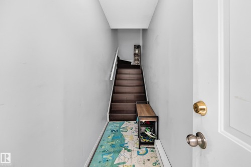 White paneled door with brass hardware opening to a hall with light gray walls and wood-finish stairs featuring a white handrail - #72 2505 42 St Nw, Edmonton, AB - Indoor Photo Showing Other Room