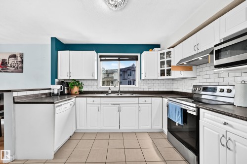 White cabinetry with brushed nickel hardware, subway tile backsplash, dark countertops, stainless steel appliances, and tiled flooring - #72 2505 42 St Nw, Edmonton, AB - Indoor Photo Showing Kitchen With Double Sink