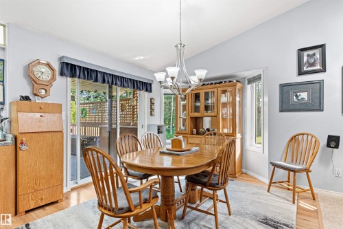 Dining space featuring a wood-finish oval table and chairs, wood-finish flooring, a contemporary chandelier, and sliding glass doors leading to an outdoor deck - #12 64 Blackburn Dr W Sw, Edmonton, AB - Indoor Photo Showing Dining Room