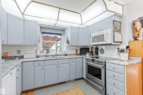 Kitchen featuring light blue cabinetry, light-toned countertops, a white tile backsplash, stainless steel range, and an over-the-range microwave - #12 64 Blackburn Dr W Sw, Edmonton, AB - Indoor Photo Showing Kitchen