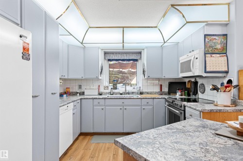 Kitchen featuring light gray cabinetry, wood-finish flooring, a white tile backsplash, and speckled countertops - #12 64 Blackburn Dr W Sw, Edmonton, AB - Indoor Photo Showing Kitchen