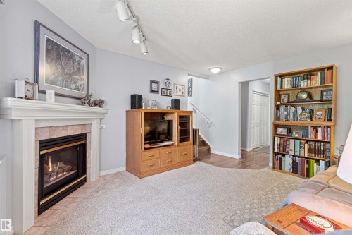 Family Room featuring a fireplace with a white mantel and tiled surround, light-colored carpeting and track lighting. - #12 64 Blackburn Dr W Sw, Edmonton, AB - Indoor Photo Showing Living Room With Fireplace