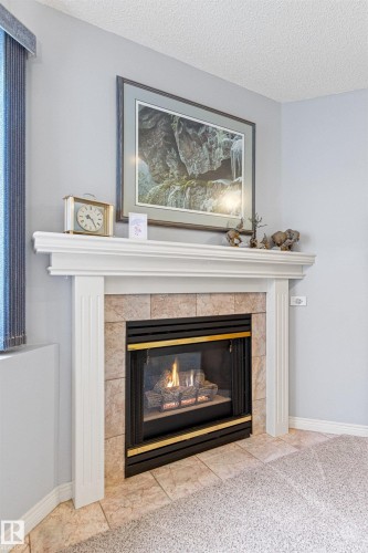 Corner fireplace featuring a white mantel, tile surround, and an integrated gas insert - #12 64 Blackburn Dr W Sw, Edmonton, AB - Indoor Photo Showing Living Room With Fireplace