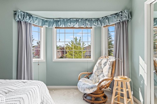 Bay window with three individual pane windows, light blue walls, carpet flooring, white baseboards, and window treatments - #12 64 Blackburn Dr W Sw, Edmonton, AB - Indoor Photo Showing Bedroom