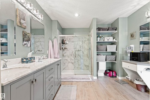 Ensuite Bathroom featuring a dual vanity with a light-toned countertop, a glass-enclosed shower with marble-look wall tiling, wood-finish flooring, shelving, and recessed lighting - #12 64 Blackburn Dr W Sw, Edmonton, AB - Indoor Photo Showing Bathroom