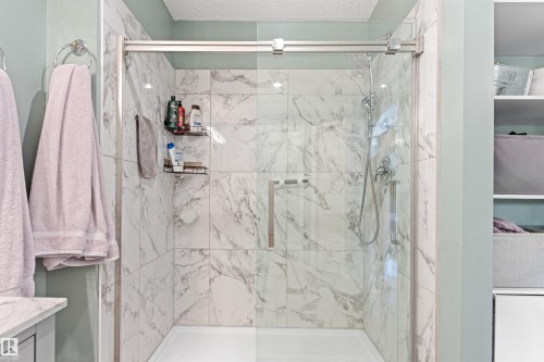 Shower enclosure featuring a frameless glass door, white marble-style tile surround, brushed nickel shower fixtures, and a white shower pan - #12 64 Blackburn Dr W Sw, Edmonton, AB - Indoor Photo Showing Bathroom