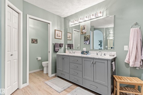 Spacious Ensuite Bathroom featuring a double vanity with stone countertops, dual sinks with chrome fixtures, and a large illuminated mirror - #12 64 Blackburn Dr W Sw, Edmonton, AB - Indoor Photo Showing Bathroom