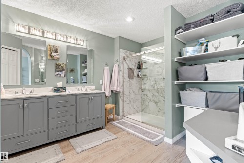 Dual vanity with a stone countertop, a glass-enclosed shower with tile surround, built-in shelving, and wood-finish flooring - #12 64 Blackburn Dr W Sw, Edmonton, AB - Indoor Photo Showing Bathroom