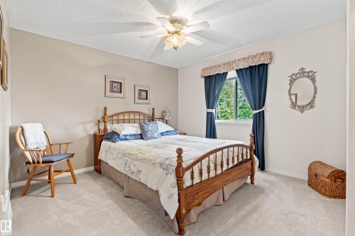 Carpeted room featuring a ceiling fan with integrated lighting, a window with exterior tree scenery, and neutral wall paint - #12 64 Blackburn Dr W Sw, Edmonton, AB - Indoor Photo Showing Bedroom