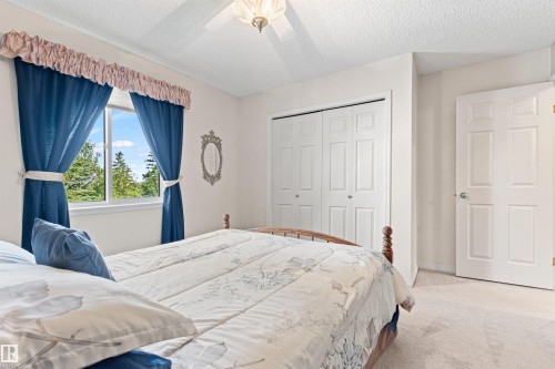 Bedroom featuring a large window, white walls, textured ceiling, light-toned carpet, and a ceiling fan with integrated lighting - #12 64 Blackburn Dr W Sw, Edmonton, AB - Indoor Photo Showing Bedroom