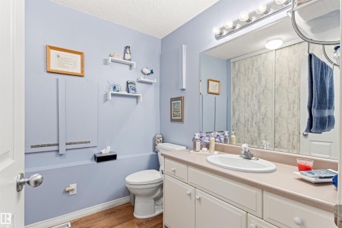 Bathroom featuring wood-finish flooring, a white vanity with an integrated sink, and a large wall-mounted mirror - #12 64 Blackburn Dr W Sw, Edmonton, AB - Indoor Photo Showing Bathroom