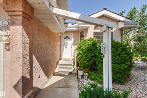 Stucco exterior featuring a white entry door with an arched transom, concrete walkway, and established perimeter landscaping - #12 64 Blackburn Dr W Sw, Edmonton, AB - Outdoor