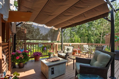 Expansive deck with retractable canopy and privacy screen, featuring a built-in fire pit, wood-finish decking, and a perimeter railing system - #12 64 Blackburn Dr W Sw, Edmonton, AB - Outdoor With Deck Patio Veranda With Exterior