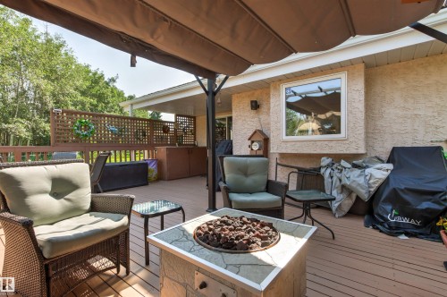 Expansive outdoor deck featuring wood-finish flooring, a built-in fire pit with a stone surround, and an overhead canopy for shade - #12 64 Blackburn Dr W Sw, Edmonton, AB - Outdoor With Deck Patio Veranda With Exterior