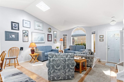 Vaulted ceilings enhance this living space featuring a large arched window, a solid entry door with an arched glass insert, light-toned carpeting, and wood-finish flooring - #12 64 Blackburn Dr W Sw, Edmonton, AB - Indoor Photo Showing Living Room