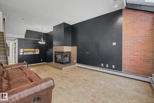 Living area featuring a corner fireplace with a tile surround and hearth, an exposed brick wall, and resilient flooring - 11150 83 Avenue Nw, Edmonton, AB 