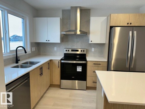 Modern kitchen featuring light wood-finish lower cabinetry, white upper cabinetry, and a light-toned backsplash - 22803 94 Anenue Northwest, Edmonton, AB - Indoor Photo Showing Kitchen With Double Sink