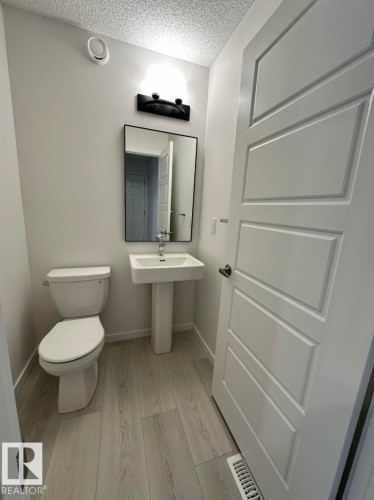 Modern powder room featuring a white pedestal sink, toilet, and light wood-finish flooring - 22803 94 Anenue Northwest, Edmonton, AB - Indoor Photo Showing Bathroom