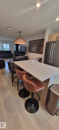 Kitchen island featuring a light-colored countertop, integrated bar seating, and light wood-finish cabinetry - 22803 94 Anenue Northwest, Edmonton, AB - Indoor Photo Showing Other Room