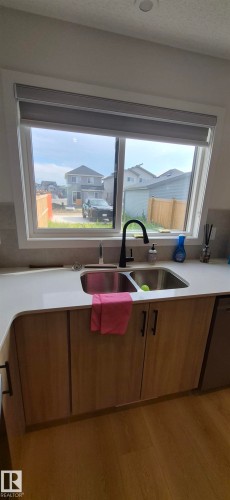 Kitchen sink area featuring a dual-basin stainless steel sink with a matte black gooseneck faucet, white countertop, light wood-finish cabinetry with black hardware, and a large window - 22803 94 Anenue Northwest, Edmonton, AB - Indoor Photo Showing Kitchen With Double Sink