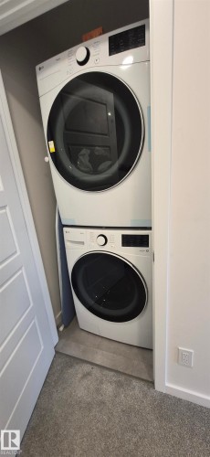 White stackable washer and dryer unit in a dedicated closet space, featuring a durable carpeted floor and a tiled utility area - 22803 94 Anenue Northwest, Edmonton, AB - Indoor Photo Showing Laundry Room