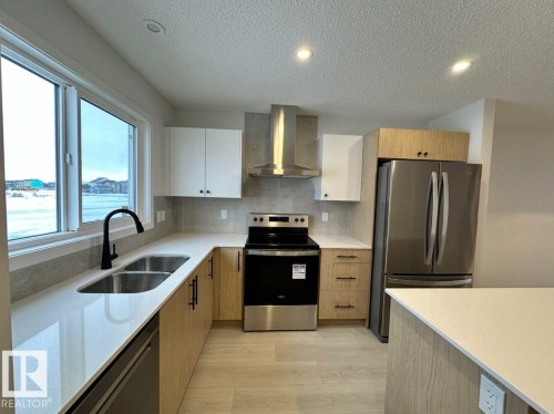 Modern kitchen featuring light wood-finish and white cabinetry, stainless steel appliances including a refrigerator, range, and built-in dishwasher, and a double basin sink with a gooseneck faucet - 22803 94 Anenue Northwest, Edmonton, AB - Indoor Photo Showing Kitchen With Double Sink