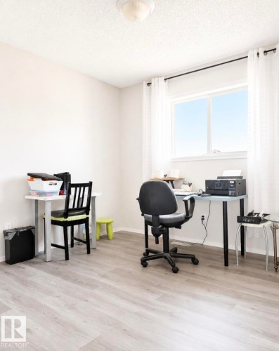 Bright interior room featuring a large window with white curtains, light wood-finish flooring, a neutral wall color, and a ceiling-mounted light fixture - 3236 27 Avenue Nw, Edmonton, AB - Indoor