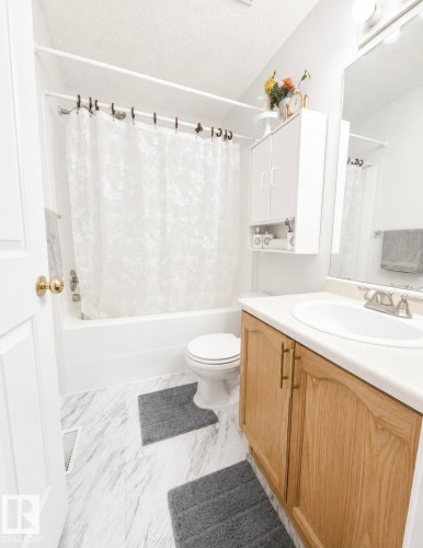 Bathroom featuring a built-in tub with shower, a vanity with a white countertop and integrated sink, a matching wall-mounted storage cabinet, and stone-look flooring - 3236 27 Avenue Nw, Edmonton, AB - Indoor Photo Showing Bathroom