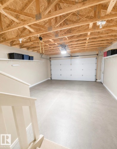 Spacious garage featuring a concrete floor, exposed wood ceiling trusses, and a white paneled garage door - 3236 27 Avenue Nw, Edmonton, AB - Indoor Photo Showing Garage